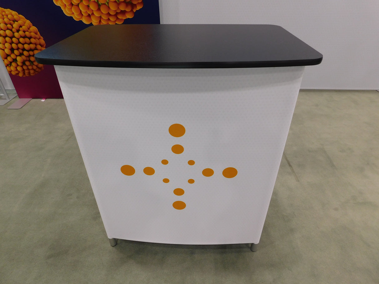 White podium with black top and orange circular design on a gray floor.
