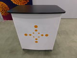 White podium with black top and orange circular design on a gray floor.